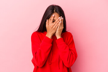 Young latin woman isolated on pink background blink at the camera through fingers, embarrassed covering face.