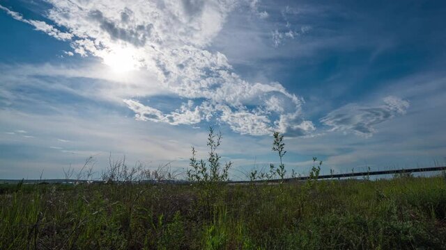 Time lapse of movement of white clouds across the blye sky. Sunset, in the evening. The movement of the camera in the grass above the river. 4K Hyperlapse