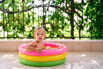 Cute baby sitting in an inflatable mini pool holding the sides