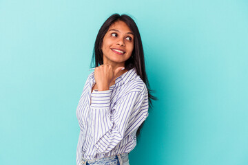 Fototapeta premium Young latin woman isolated on blue background points with thumb finger away, laughing and carefree.