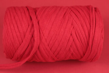 Skein of twisted red cotton thread.Knitwear yarn coil texture closeup on red background.Crochet and knitting, hobby concept.Place for your text.