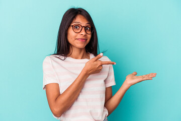 Young latin woman isolated on blue background excited holding a copy space on palm.