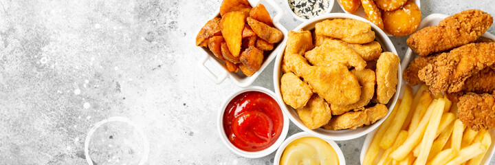 Chicken nuggets, strips, french fries, fried potatoes, ketchup and cheese sauce on a light background. Fast food top view with copyspace. Banner	