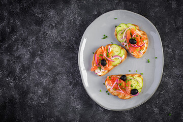 Toasts with cream cheese, smoked salmon, cucumber, black olives and red onion. Open sandwiches. Healthy care, super food concept. Top view, overhead