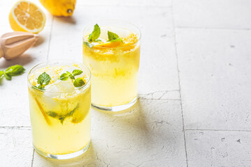 Homemade lemonade with mint and ice in glasses, gray tiles background.