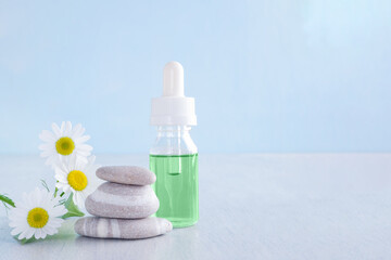 green liquid in a glass bottle with chamomile and stones