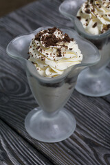 Dessert with cream and blueberries. Decorated with chocolate drops. In glass goblets. On black pine boards.