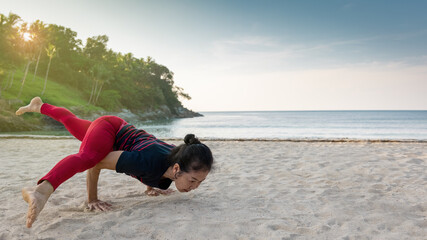 Strong asian senior woman do one legged arm balance Hurdler yoga pose at the sandy beach with blue sky and beautiful sea in the summer of Phuket, Thailand. Sport active lifestyle and healthy concept.