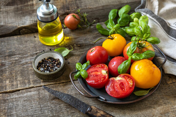 Fresh raw ripe organic yellow, red tomatoes and ingredients for cooking salad on a wooden table. Copy space.