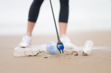 Contamination of wildlife with plastic and other debris. A volunteer removes plastic bottles from the shore with a special stick. Minimalism. Low angle view.Blurred background.