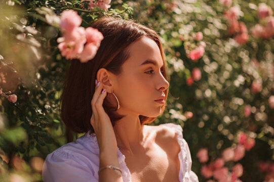 Fototapeta Summer street style, fashion portrait of beautiful brunette woman with elegant bob hairstyle,  wearing white blouse, posing in street, near blooming roses. Copy, empty space for text 
