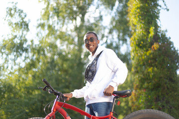 A happy African-American man is walking down the street with a bicycle