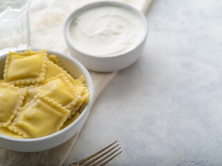 Restaurant dish. Homemade dish - ravioli and sour cream. Ravioli and sour cream stand in deep white bowls on a white background. There are no people in the photo. Place for your insert.