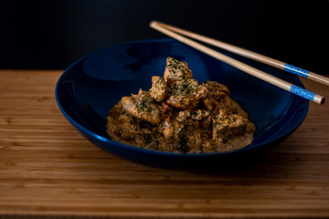 Mouth watering chicken butter masala curry in a blue bowl garnished with green chopped leaves with a wooden background