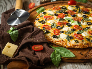 Beautiful composition. On a wooden table - pizza, knife, brown napkin, cheese, a slice of tomato,...