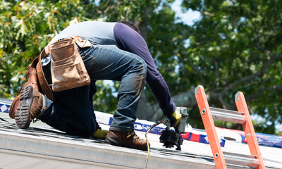 Contractor using nail gun replacing roof shingles on a roof