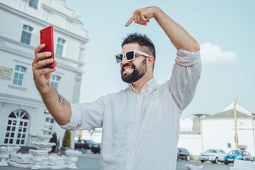 Young beard handsome man make selfie photo on smartphone, hipster style, street, sunglasses, happy face