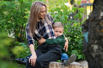 Naklejka na ściany i meble Portrait of nice young mother with pleasure spending time with precious son in Backyard. Vacation. Hugging lovely mom, having fun together, happy family enjoying life