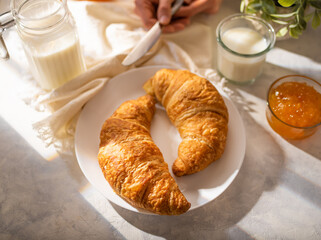 Morning traditional breakfast consisting of two croissants on a white plate, milk and orange jam....
