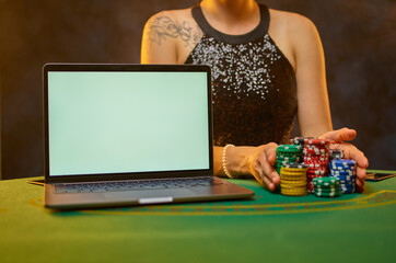 Gambling. Online casino. A virtual reality. Risk and chance to win or lose money. A young woman in a beautiful dress sits at the poker table. There is an open laptop next to it and a lot of chips.