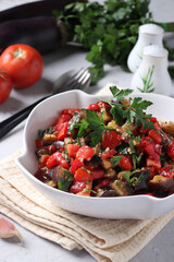 Salad with eggplants, tomatoes, garlic and parsley in a white bowl on a light gray background. Close-up