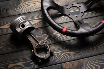 Car tuning concept flat lay background. Car piston and sport steering wheel on the wooden workbench...