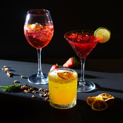 Aperol Spritz and red and yellow aperitif cocktails in glass with ice on black background