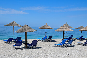Strand mit Stroh-Sonnenschirm und blauen Liegestühle und Blick aufs Meer bei Himara in Albanien