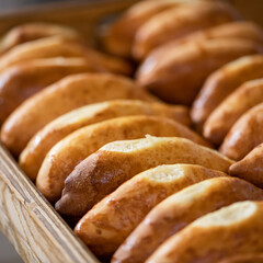 Rows of patties or pies on wooden tray. Close-up shot. Soft focus. Fresh baking, cooking process.