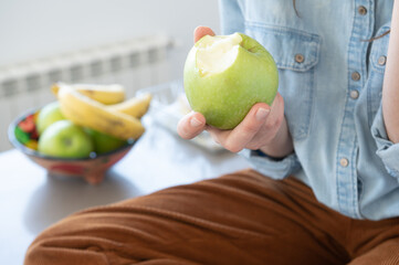 Close up of woman's hand holding a healthy and tasty green apple.In blurred background container with fruits.Healthy food