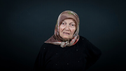 Portrait of a Turkish senior Muslim woman with black background. She is nervous, tense and unhappy