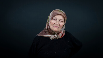 Portrait of a Turkish senior muslim woman with black background. She has a happy smiling expression...