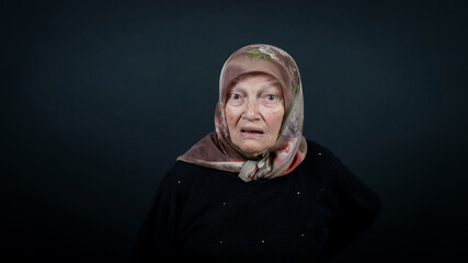 Portrait of a Turkish senior Muslim woman with black background. She is surprised, scared and shocked.