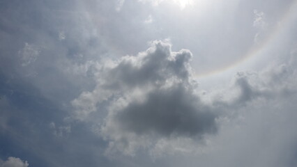 Dark rain clouds in blue sky with rainbow pattern observed in Sun's halo