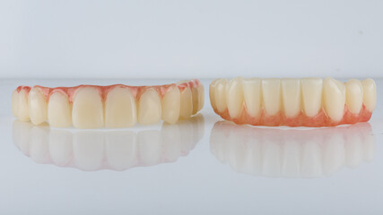 Two temporary dental prosthesis of polymer and pink gum top and lower jaws on a white background