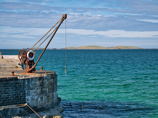 An abandoned, rusting steel crane and winch at the side of a pier in Portrush, Northern Ireland, UK...
