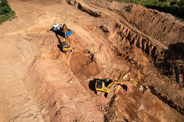 Obraz premium Excavator load the sand into dump truck. Aerial view of an backhoe on earthworks. Open pit development and sand mining. Loader digging ground for foundation pit. Earthmoving at construction site.