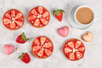 Delicious small tartlet pastries topped with strawberry fruits and white chocolate sprinkles next to coffee cup