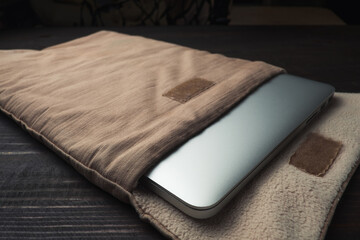 Laptop in a soft textile case, on the wooden table. 