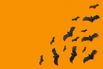 A lot of black bats flying on an orange background. Scary halloween flat lay composition on an orange background. Halloween decoration concept