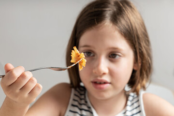 Cute litte girl eating pasta with tomato sauce with isalate gray background