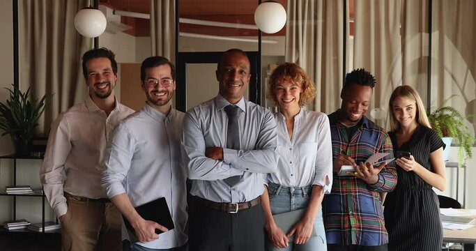 Six diverse multiracial professional business team portrait. Young company employees members led by African middle-aged boss standing in row in office pose on camera. Unity, career, equality concept