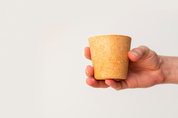 Male hand holding eco-friendly waffle coffee cup on neutral background with copy space. Alternative...