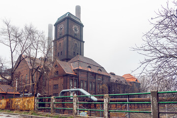 Old, coal power plant in Szombierki district in Bytom, Silesia, Poland. Industrial, brick building with clock tower and chimneys on a foggy day.
