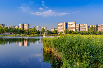 Fototapeta na wymiar View at Tysiaclecie district in Katowice on a beautiful, sunny day, seen through the pond. Apartment buildings situated neat the lake against blue sky.