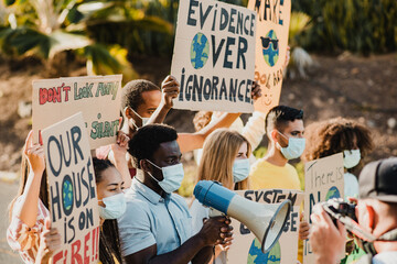 Young multiracial demonstrators protesting for climate change while wearing safety masks outdoor in...