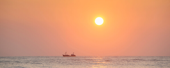 silhouette of fishing ship under orange sky during sunset at sea