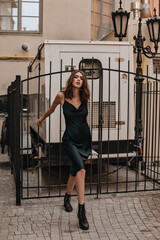 Full-length portrait of stylish young brunette in dark green silk long dress and high black shoes,...