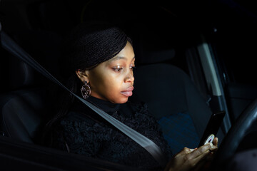 African lady sitting in the car at night chatting on mobile phone.