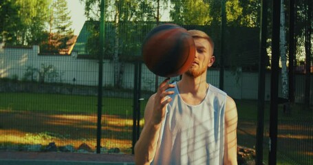 Male basketball player young cool guy spinning a ball on finger on basketball court outdoors in sunshine